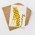 A greeting card with a yellow leopard design and black dots is placed on a brown envelope against a white background.