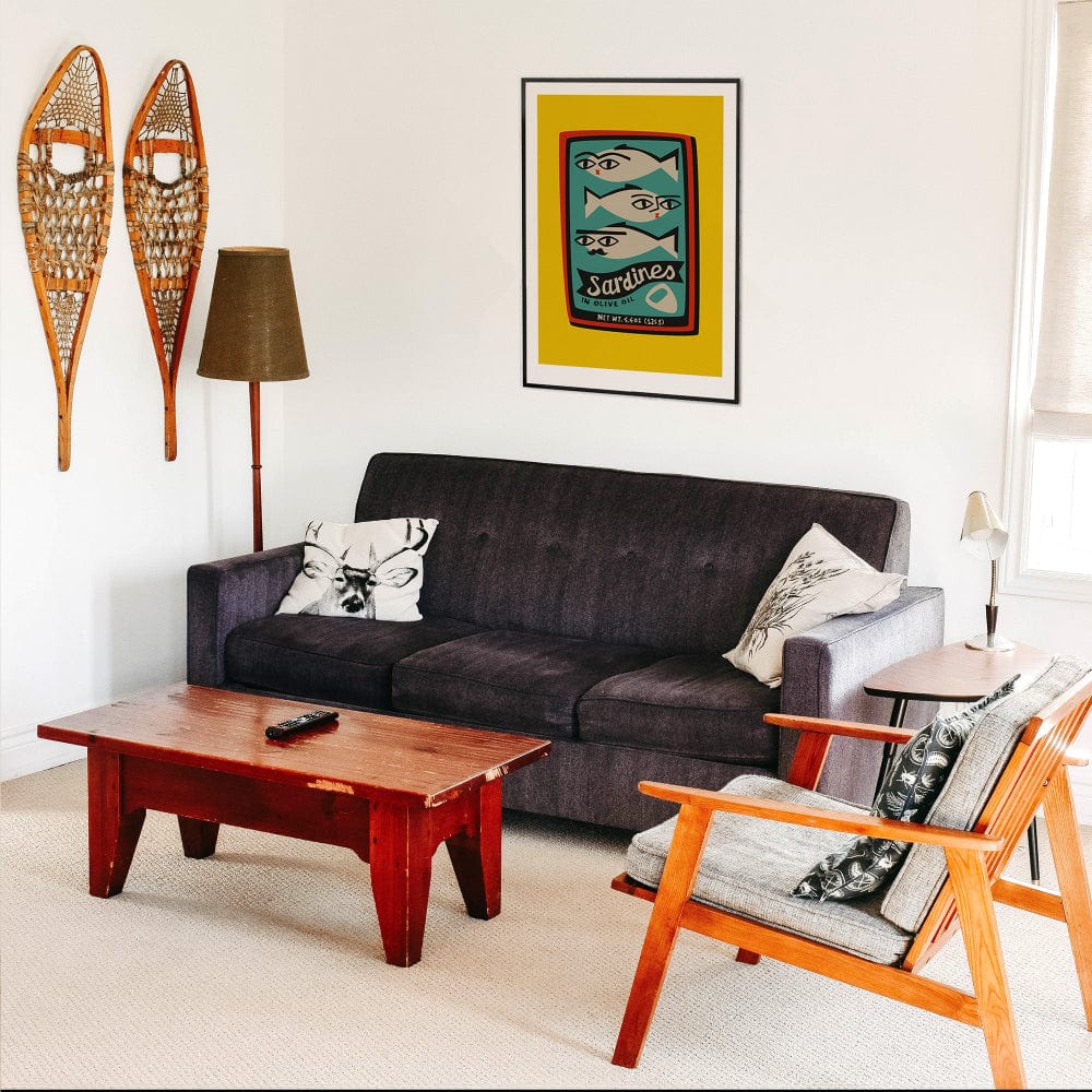 Sardines print framed above a black sofa in a mid-century styled living room with wooden furniture.