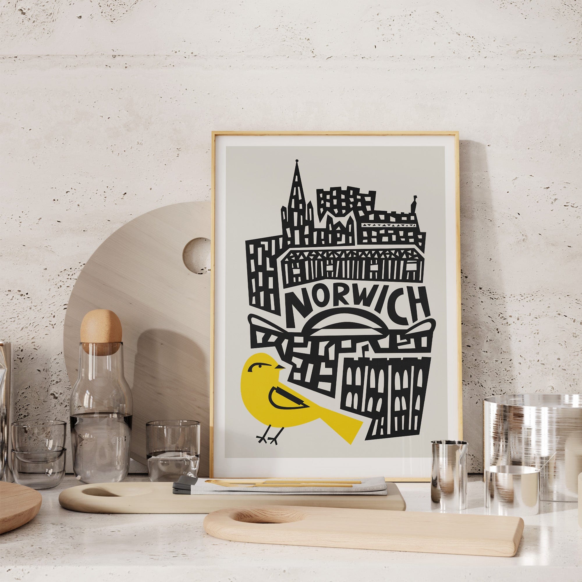 Norwich city poster styled on textured wall above light wood dining setup with glassware and ceramics