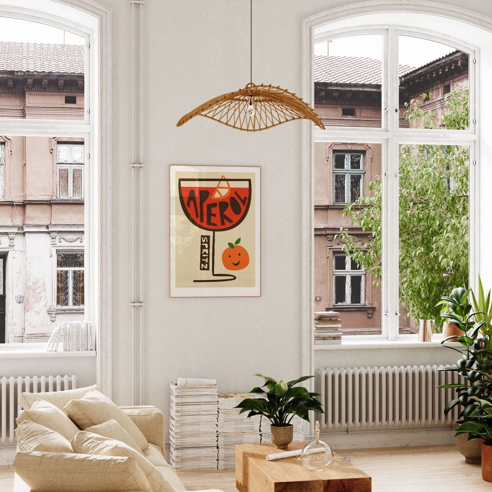 Retro-style Aperol Spritz poster framed in a bright apartment, beside greenery and classic windows.
