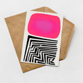 a card with a pink square and a black and white geometric pattern on it, placed on top of a brown envelope.