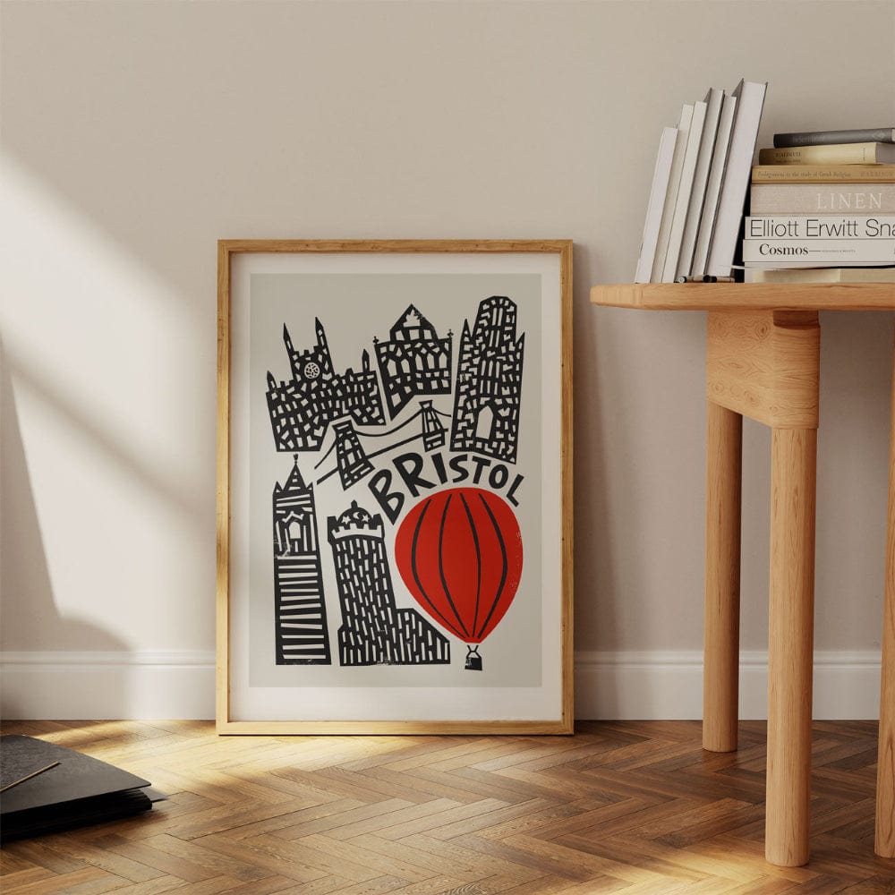 Bristol city print with a red balloon, leaning casually on a wooden desk in a bright modern interior.
