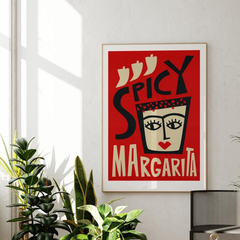 The Spicy Margarita print brings fire and flair to a minimalist room, framed in black and glowing in natural sunlight against a clean white wall.