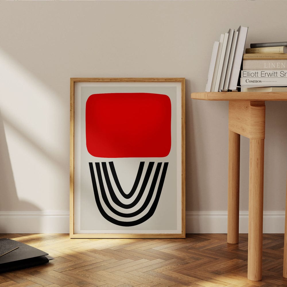 Red abstract print styled leaning against a wall next to wooden desk in modern interior