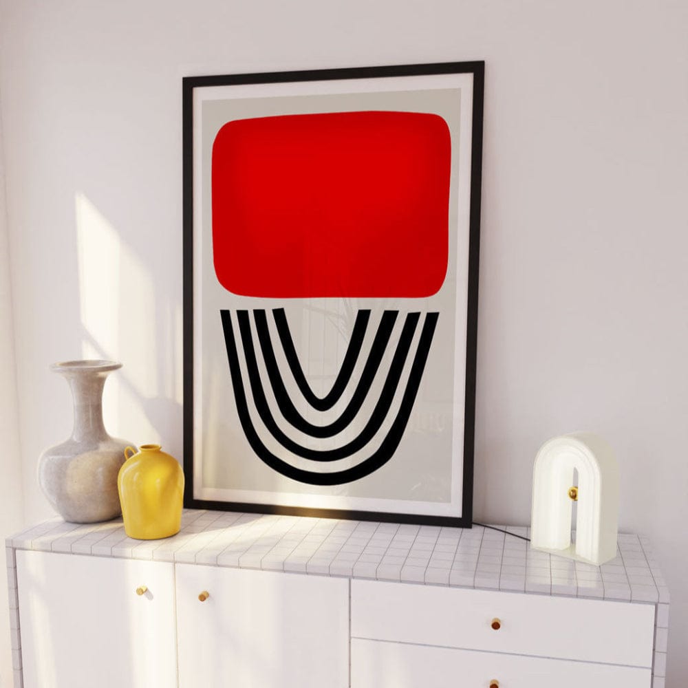 Red and black abstract arch print framed above white sideboard with neutral ceramic accents