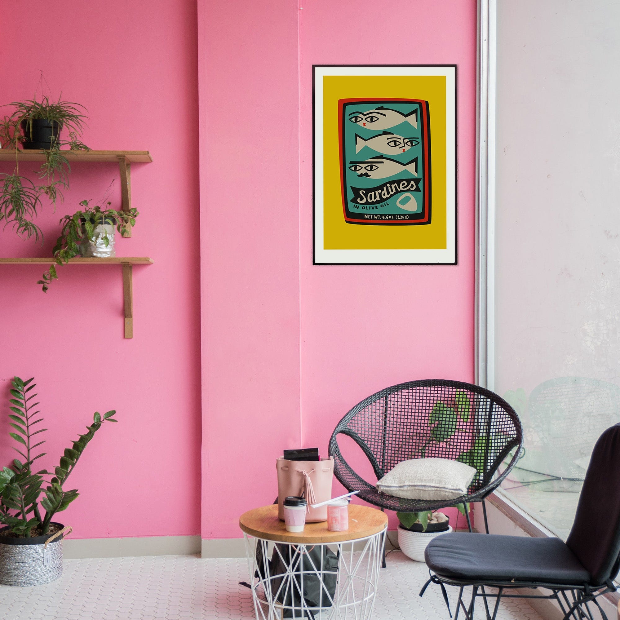 Sardines poster framed on a pink wall above a small table and wire chair in a colourful modern space.