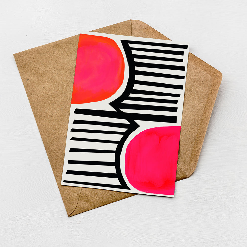 a card with a bold, abstract design in black and white, with a vibrant red circle on the right side. The card is placed on top of a brown envelope, which is set against a white background.