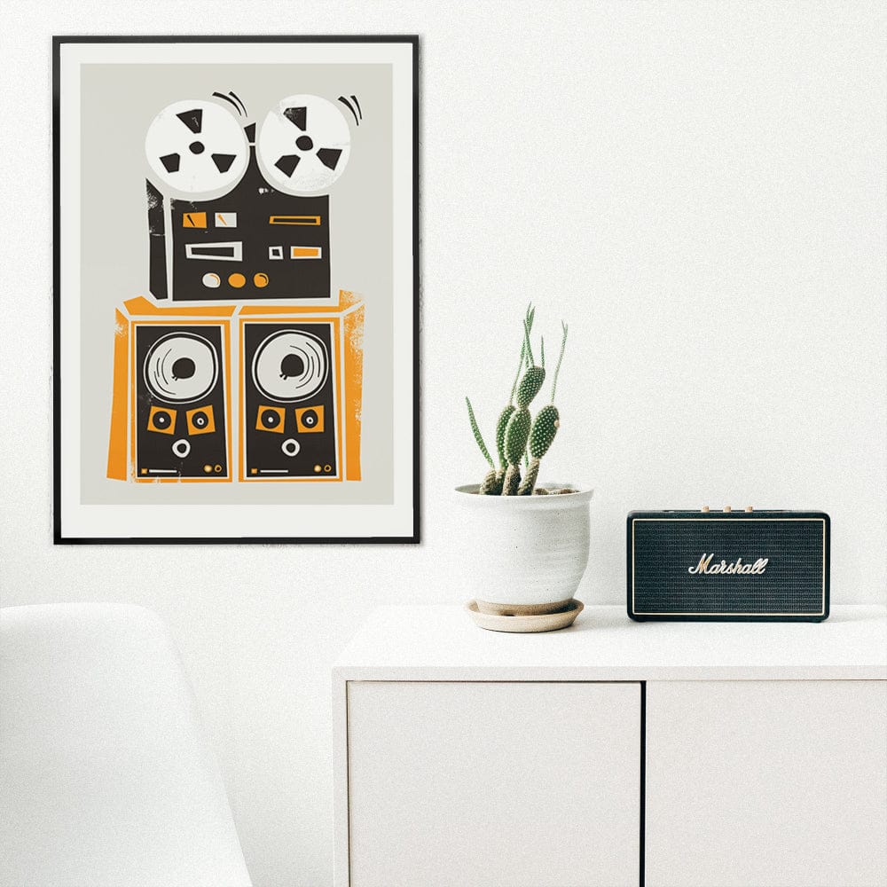 Retro tape deck print hanging above a white desk with potted plant and black Marshall speaker in a minimalist interior