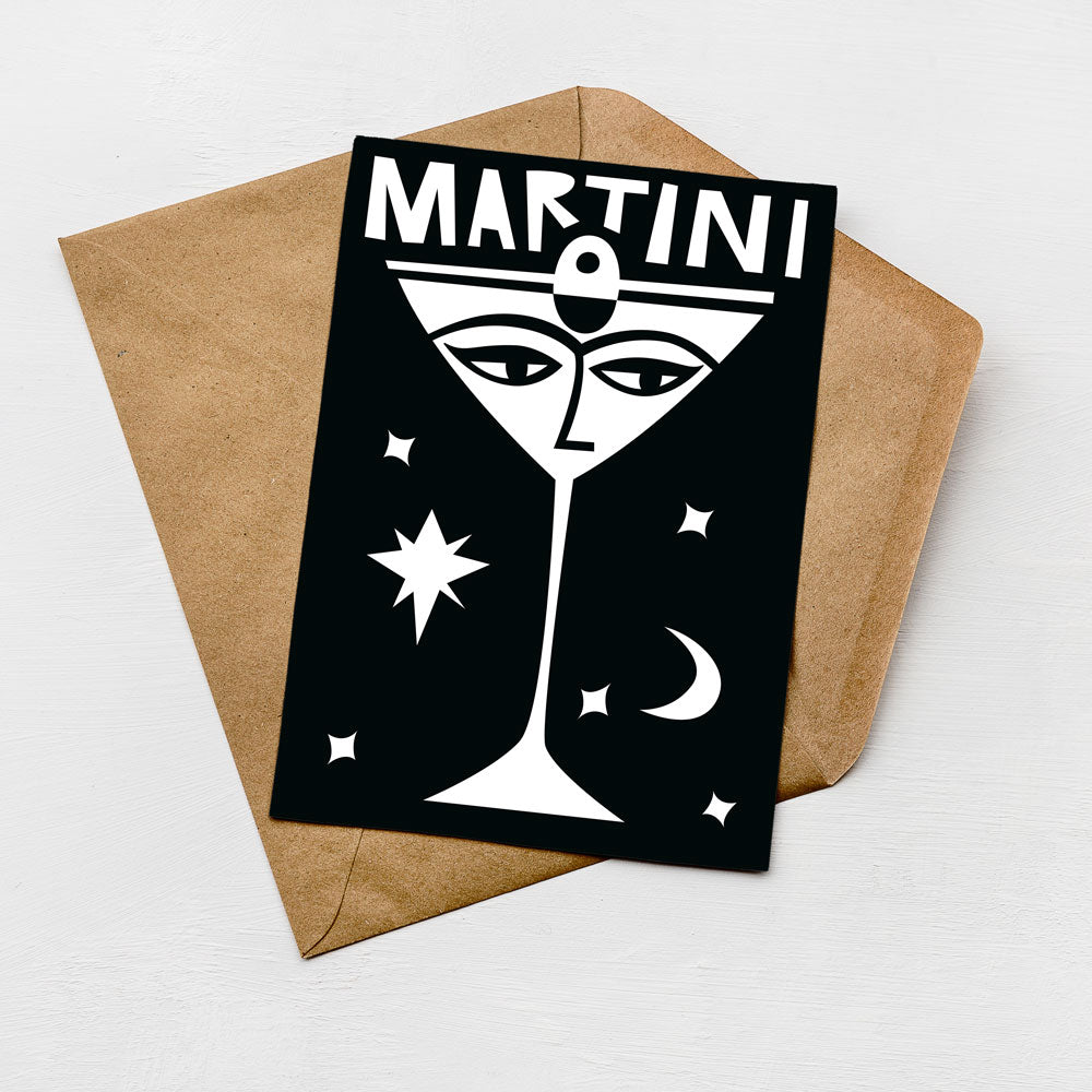 A card with a stylized illustration of a martini glass and stars on a black background, placed on top of an envelope.