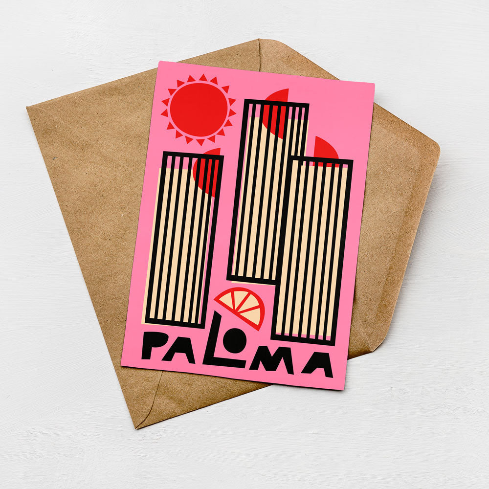A pink card with a stylized design featuring a sun, buildings, and a slice of lemon, placed on top of a brown envelope.