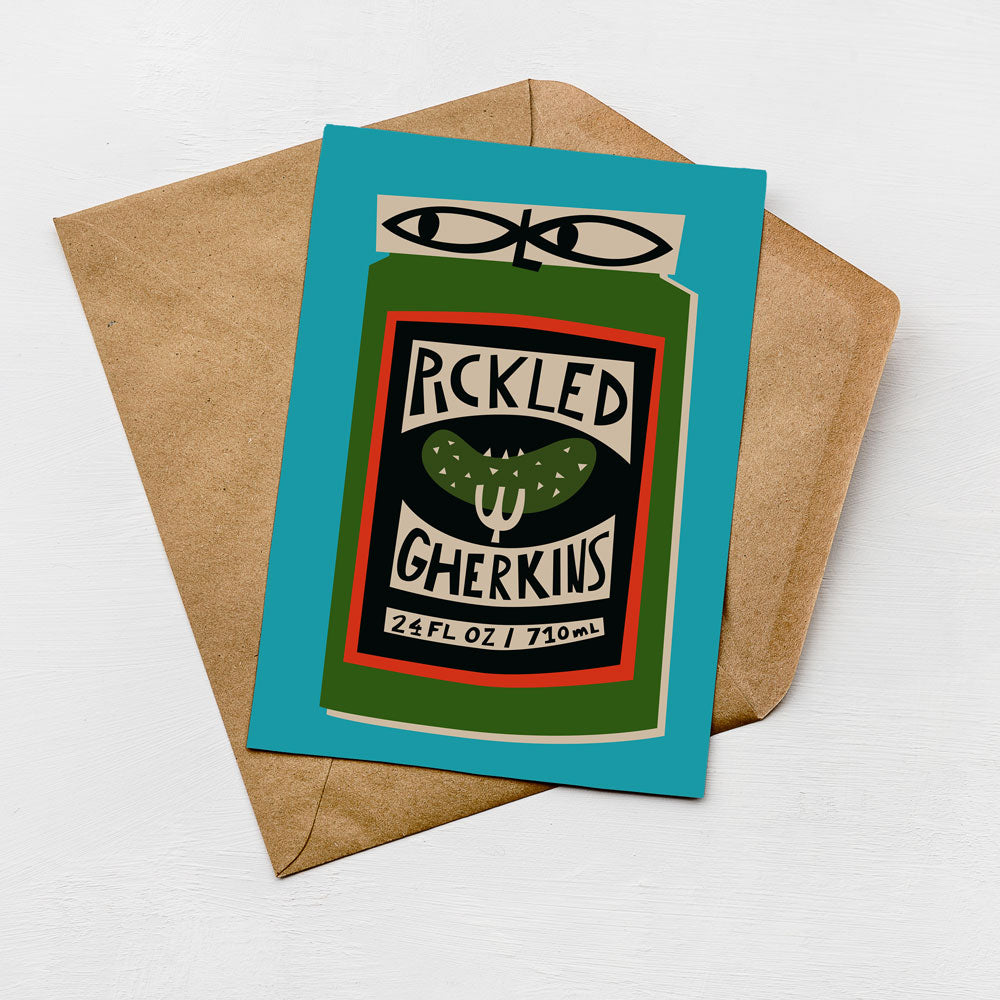 A card with a graphic design featuring a can of pickled gherkins, placed on top of a brown envelope against a white background.