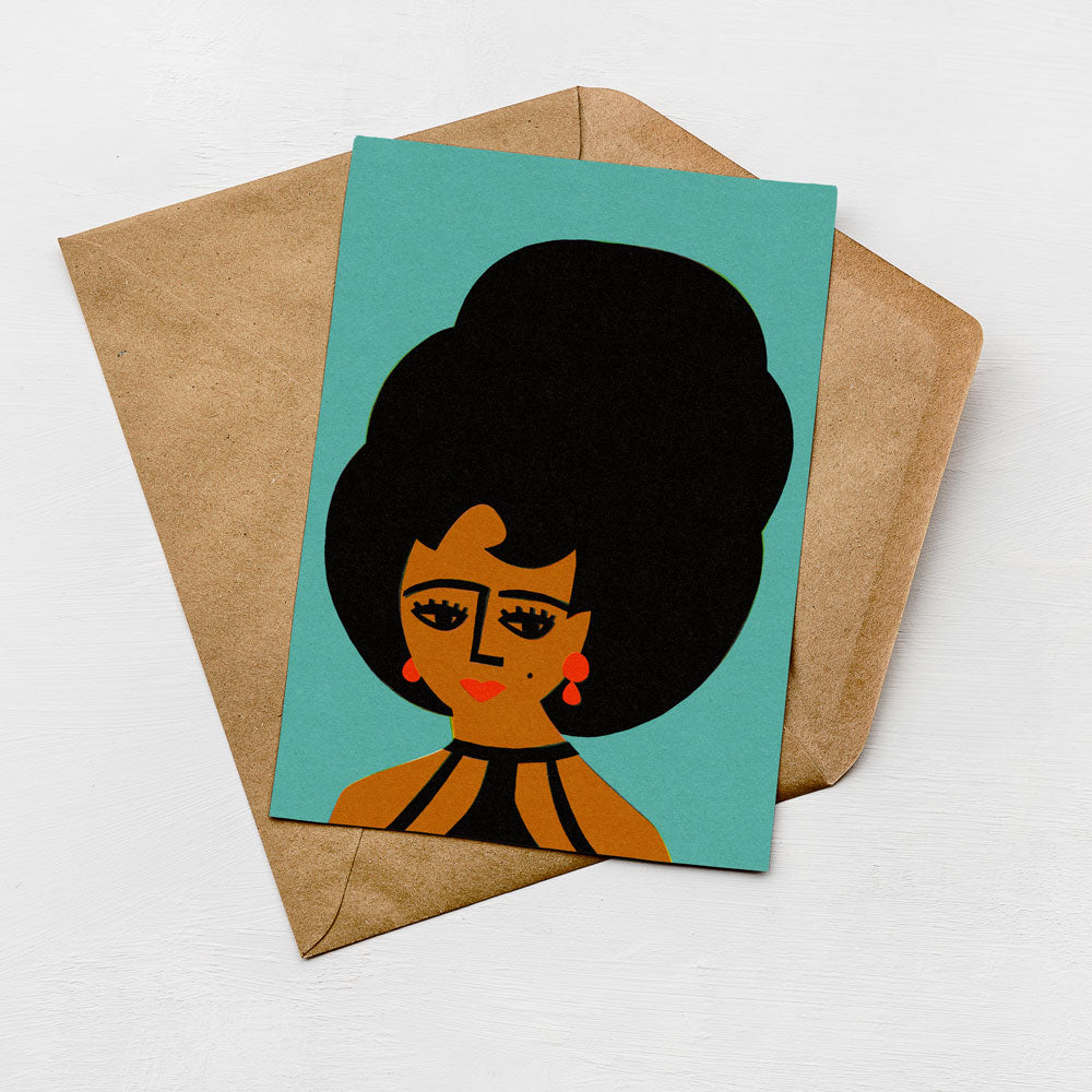 A card with a stylized illustration of a woman's face on a turquoise background, placed on top of a brown envelope.