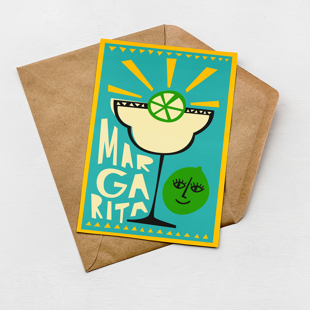 A colorful greeting card with a stylized illustration of a margarita glass and a lime, placed on a brown envelope against a white background.
