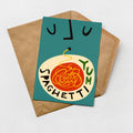 A greeting card with a colorful illustration of spaghetti and the words "YUM SPAGHETTI" printed on it, placed on a brown envelope against a white background.
