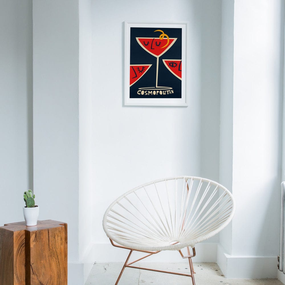 Cosmopolitan print hanging in a minimalist white room with a curved chair and natural wood elements for contrast.