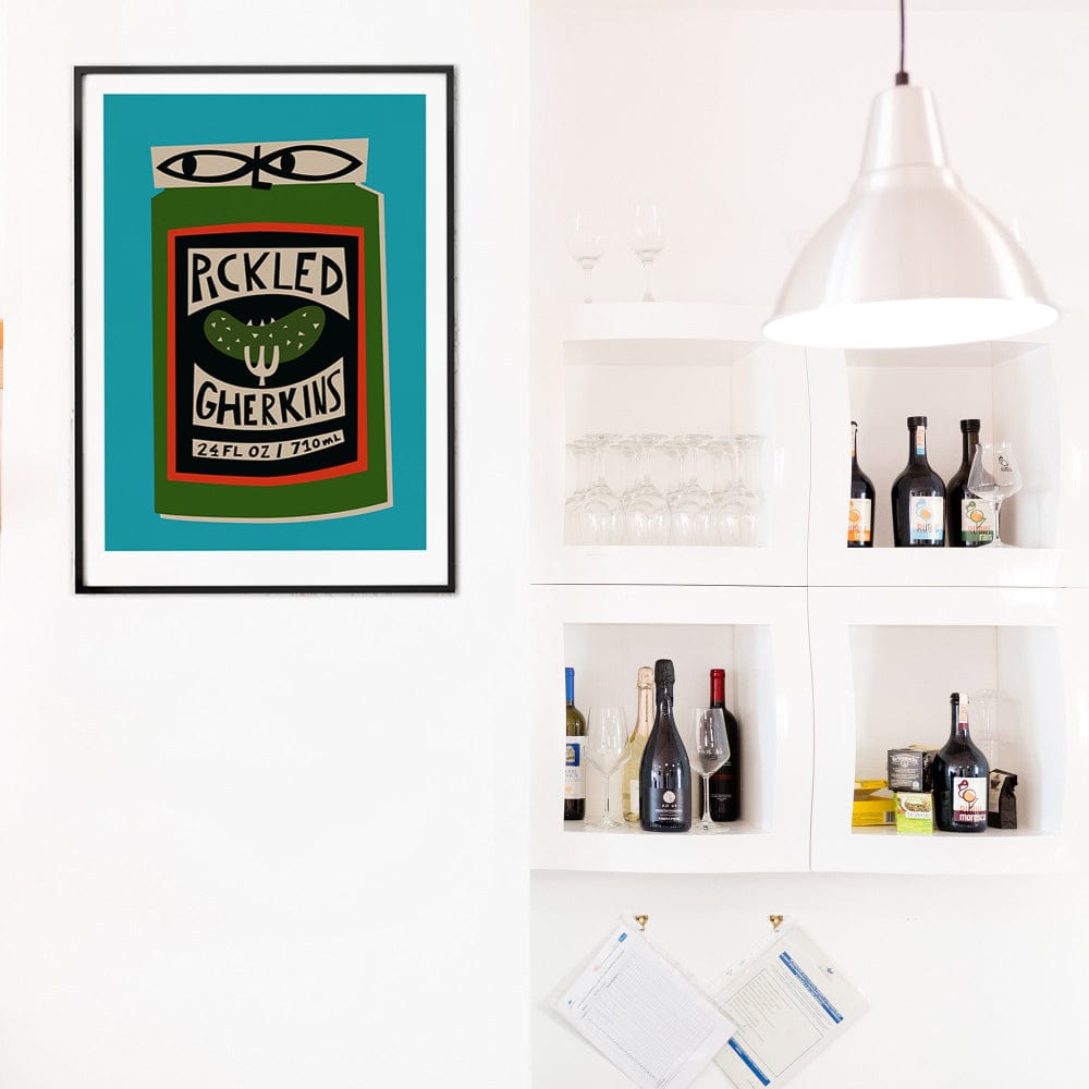 Pickled Gherkins poster framed above a bar cart and open shelving in a white modern kitchen.