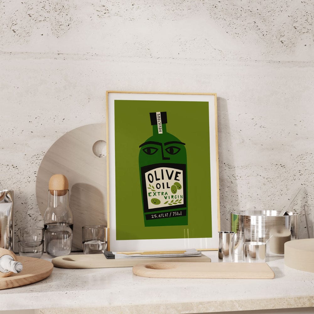Framed olive oil bottle print styled on a stone-textured kitchen wall with wooden utensils and glassware.