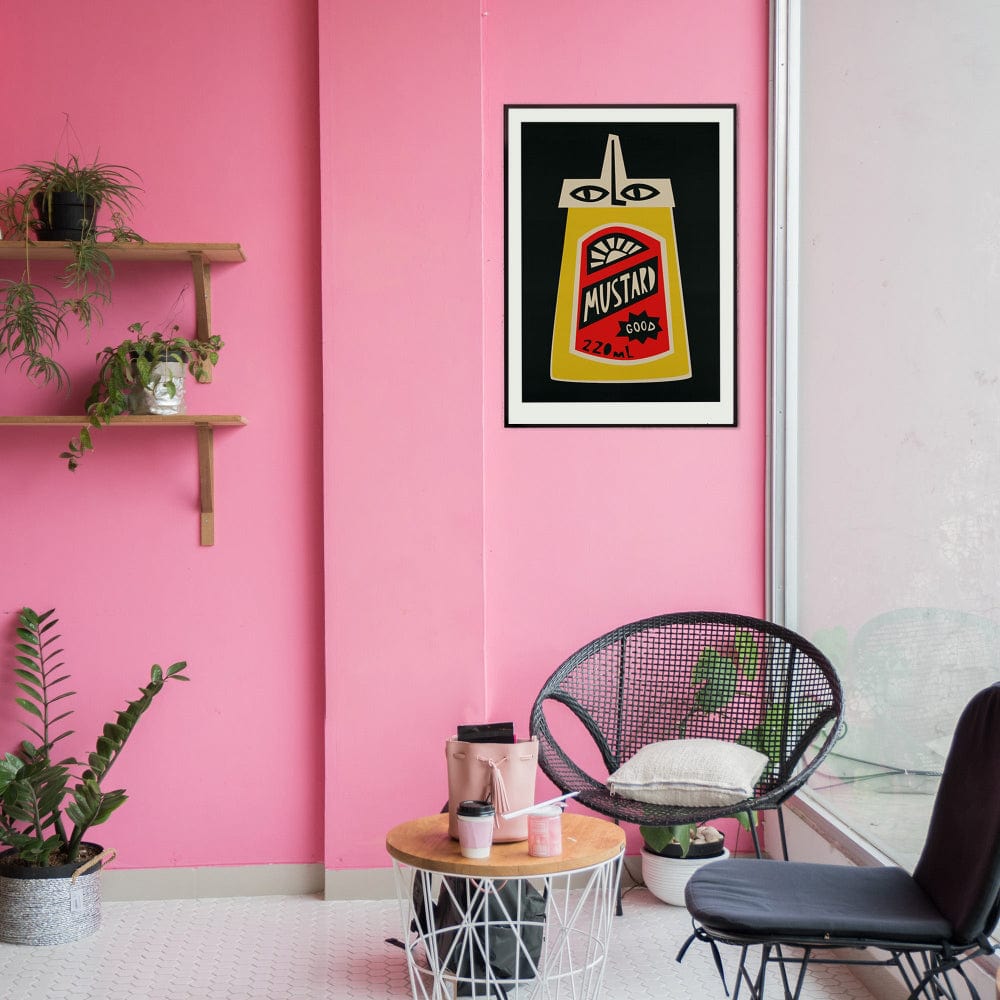 Mustard artwork framed on a pink wall in a playful studio space with black wire chair and potted plant.