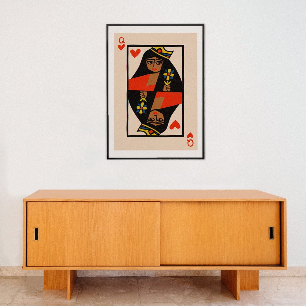 Queen of Hearts playing card print framed above minimalist wooden sideboard on white wall.