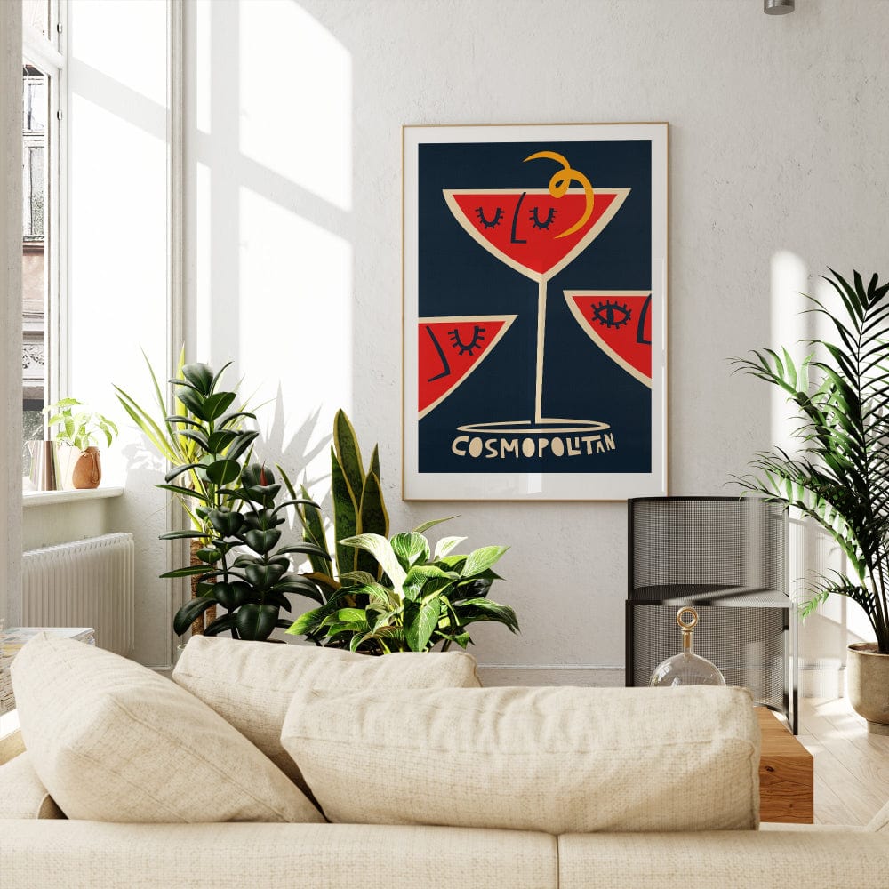 Cosmopolitan cocktail poster framed in a sunlit living room with tall windows, a white sofa, and leafy green accents.