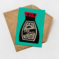 A card with a soy sauce bottle illustration on it, placed on a brown envelope against a teal background.