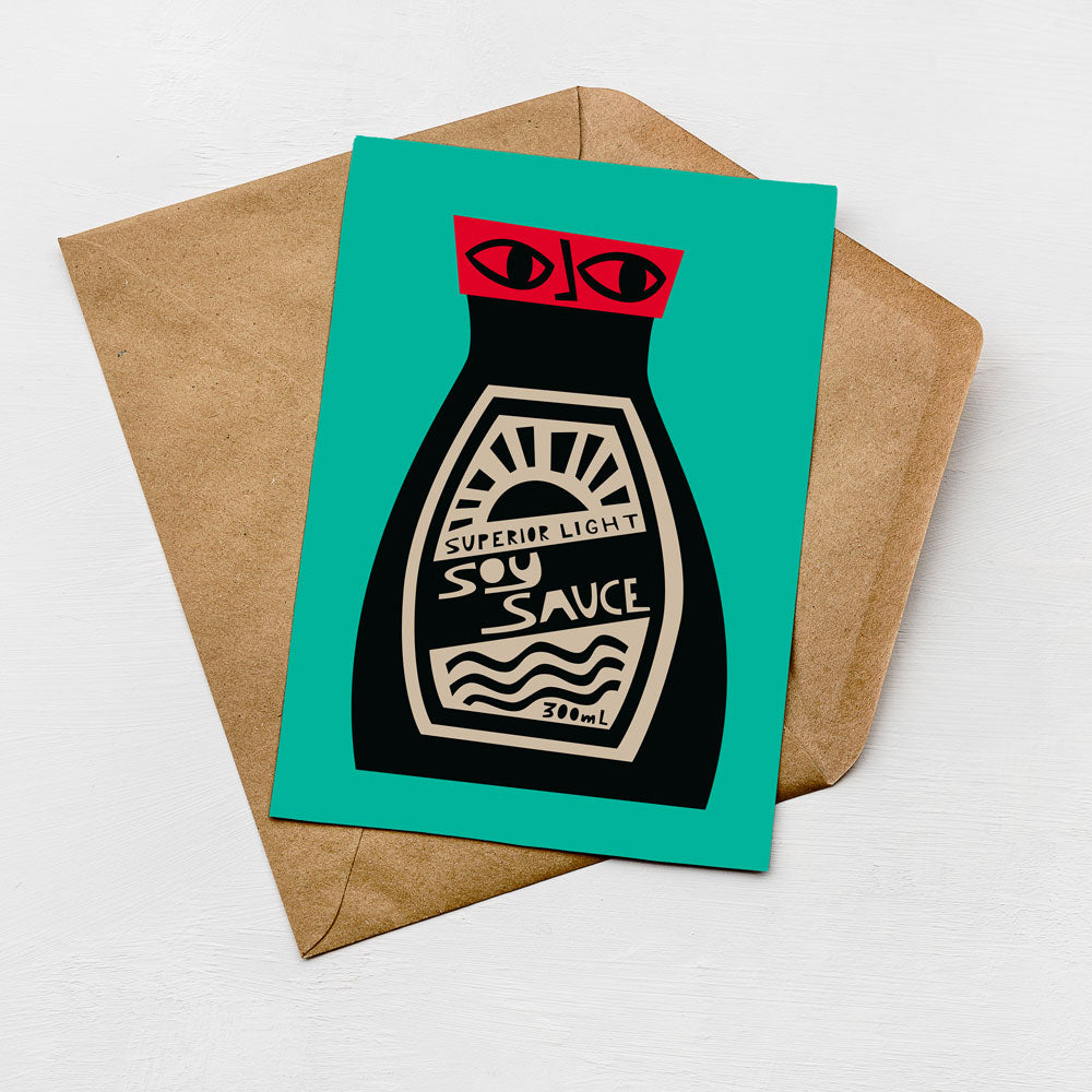 A card with a soy sauce bottle illustration on it, placed on a brown envelope against a teal background.