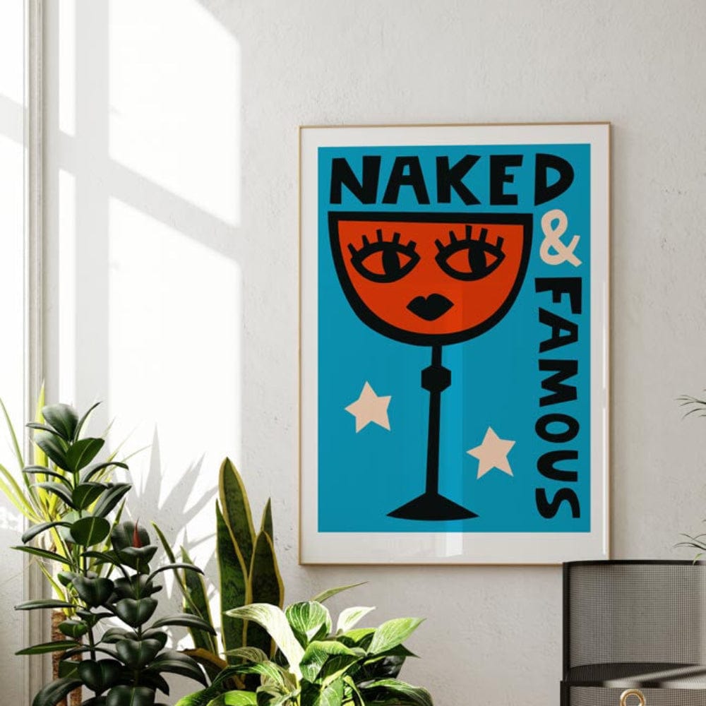 The Naked & Famous print displayed in a bright room with white walls and natural light, framed in black and surrounded by fresh greenery.