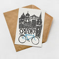 A card featuring a stylized illustration of a city skyline with a blue bicycle in the foreground, placed on top of an envelope.