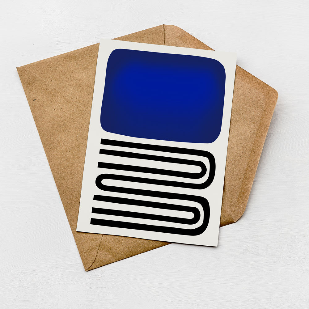 a card with a blue square and a black and white abstract design on it, placed on top of a brown envelope.