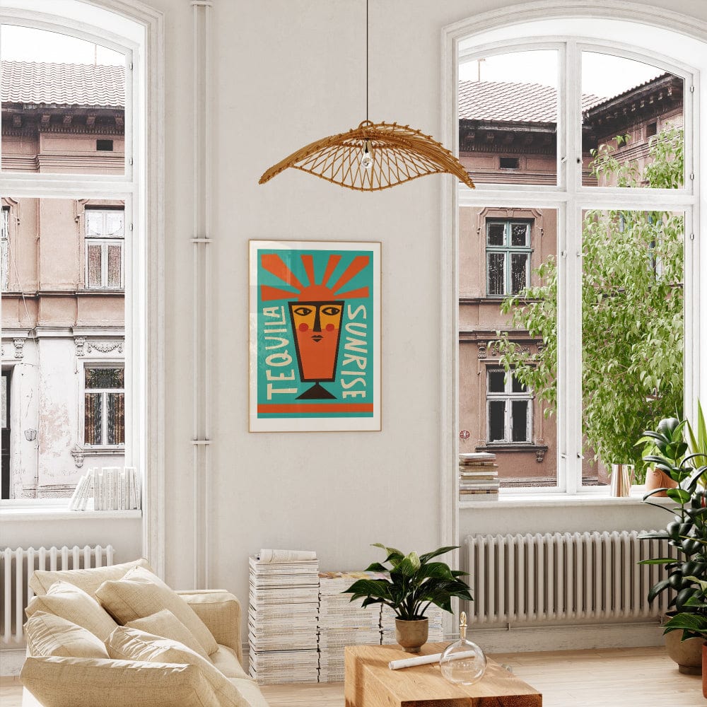 Tequila Sunrise print framed on a white wall in a bright interior with tall windows and leafy indoor plants.