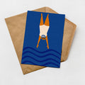 A greeting card with a blue background and a swimming illustration is placed on top of a brown envelope.