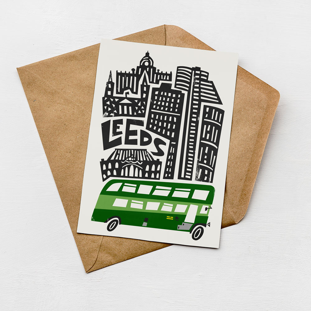 A greeting card featuring an illustration of a city skyline with a green double-decker bus in the foreground.