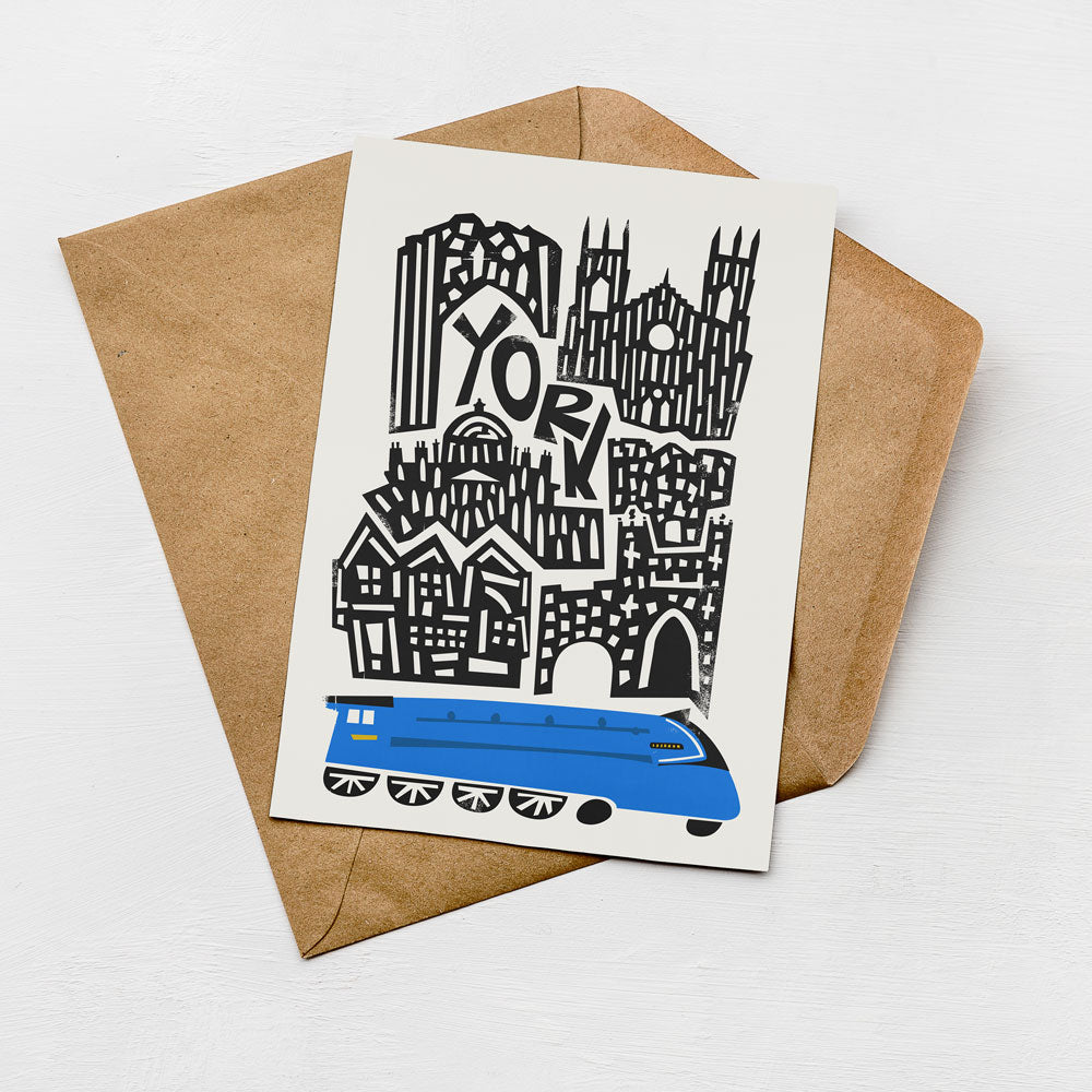 A card with a stylized illustration of a city skyline and a blue train on top of it, placed on a brown envelope.