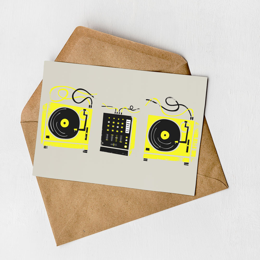 A greeting card with a design featuring two turntables and a control panel, along with a brown envelope on a white background.