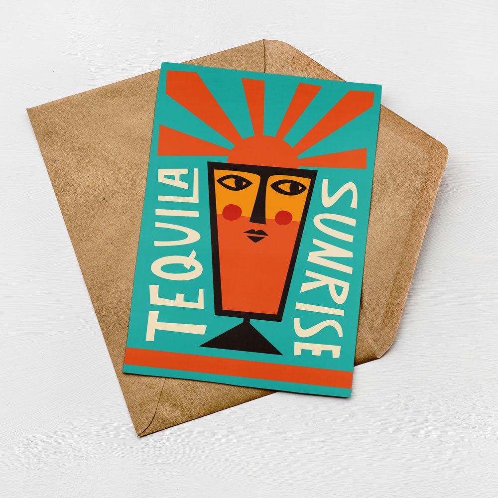A colorful greeting card with a stylized illustration of a face and the text "TEQUILA SUNRISE" on it, placed on a brown envelope against a white background.