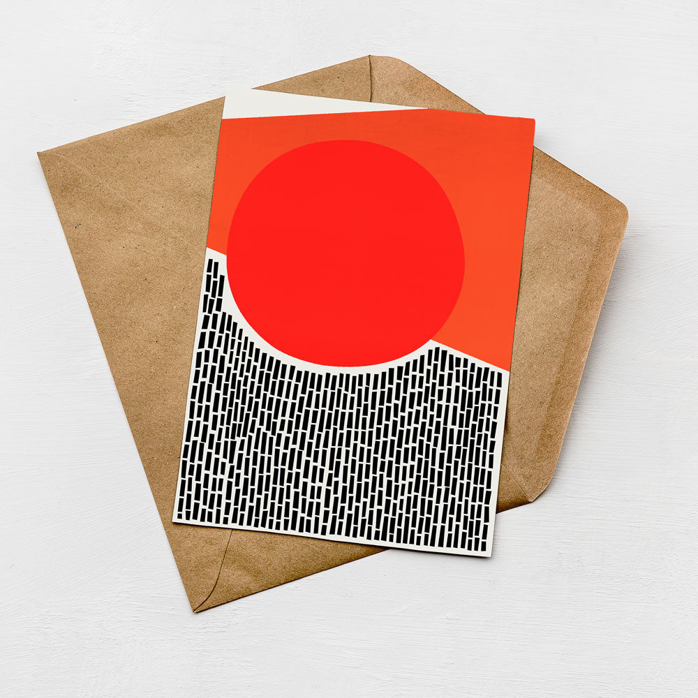 a card with a red circle and a black and white geometric pattern on it, placed on top of an envelope.