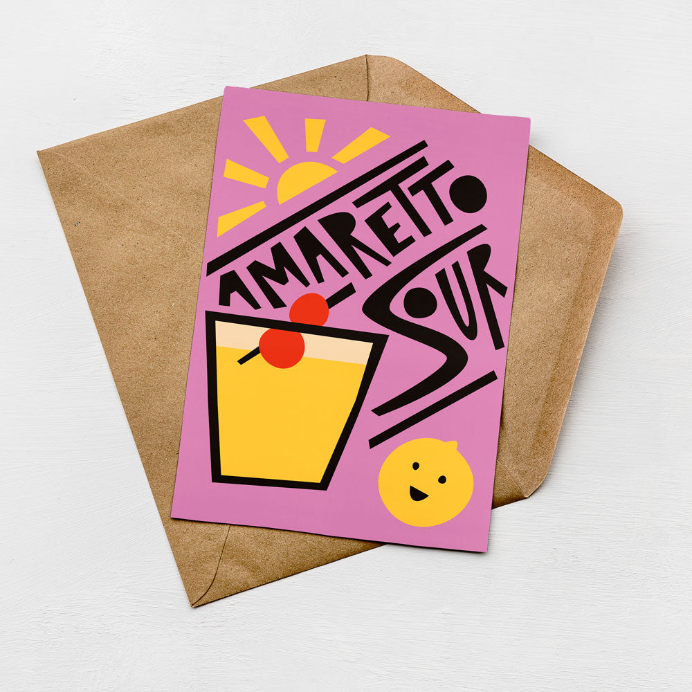 A colorful greeting card with a stylized illustration of a cocktail glass and a lemon, along with the text "AMARETTO SOUR" written in a playful font.