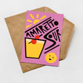A colorful greeting card with a stylized illustration of a cocktail glass and a lemon, along with the text "AMARETTO SOUR" written in a playful font.