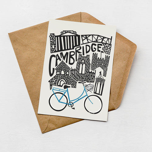 A greeting card featuring an illustration of a cityscape with a bicycle, placed on a brown envelope against a white background.