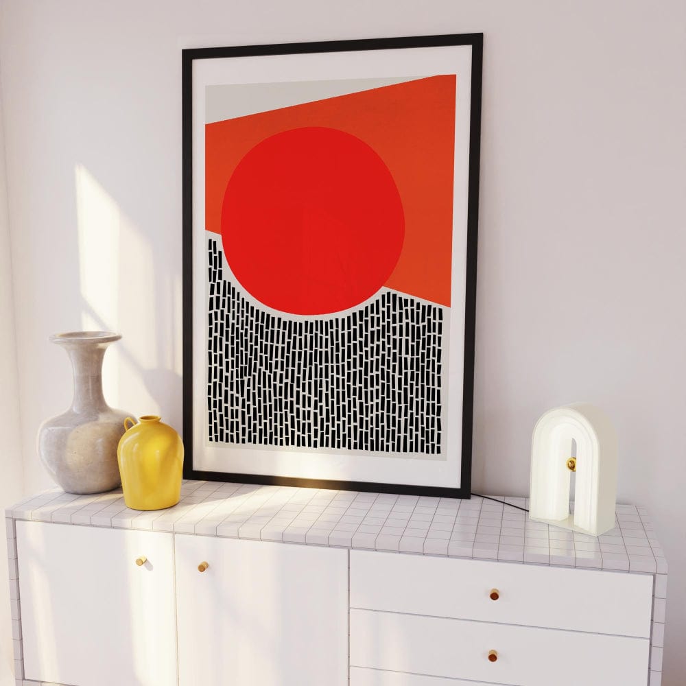 The red circle abstract artwork framed and propped on a shelf, bringing colour and energy to a minimalist setting with sculptural vases and soft lighting.